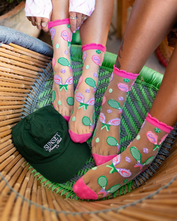 Sheer socks with tennis racket design worn by a person sitting on a woven chair.