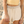 A woman standing on a sandy beach wearing a pale yellow ribbed short-sleeve crop top with light blue trim and cream drawstring shorts.