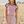 A woman standing on a sandy beach wearing a light pink ringer crop top with black trim and matching light pink drawstring shorts.