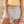 A woman standing on a sandy beach wearing a pale yellow ringer crop top with light blue trim and light gray ribbed shorts.