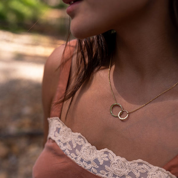 Close-up of a person wearing a gold necklace with interlocking rings, blurred natural background