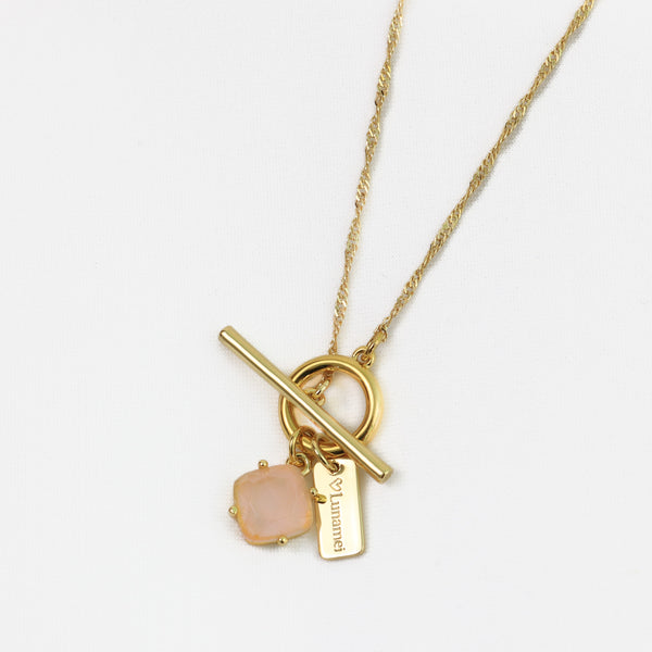 Gold necklace with a pink stone and tag on a white background