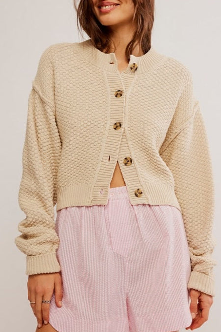 Woman wearing a beige cardigan and pink shorts on a plain background