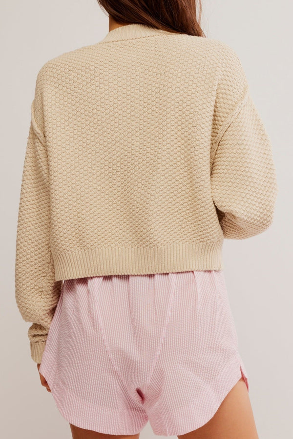 Person wearing a beige textured sweater and pink shorts on a plain background