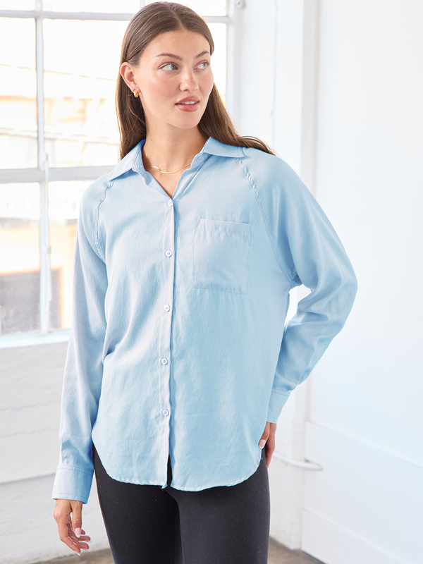 Woman wearing a light blue button-up shirt in a bright room.