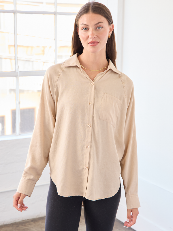 Woman wearing a beige button-up shirt in a bright room