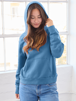 Woman wearing a blue hoodie in a bright room with large windows.