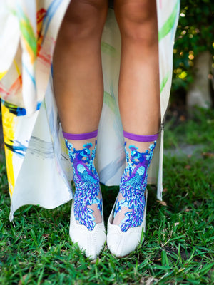 Person wearing colorful socks with a blue peacock pattern on grass
