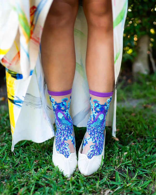 Person wearing colorful socks with a blue peacock pattern on grass