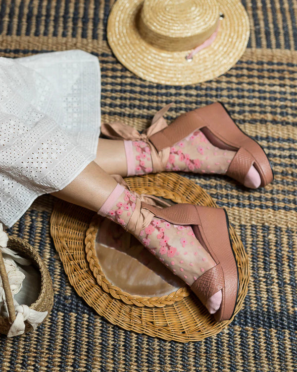 Brown sandals with pink floral designs worn by a person on a textured surface.