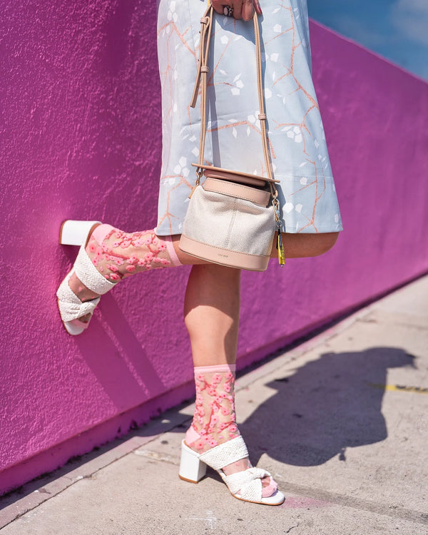 Person wearing pink patterned socks and white sandals against a pink wall.