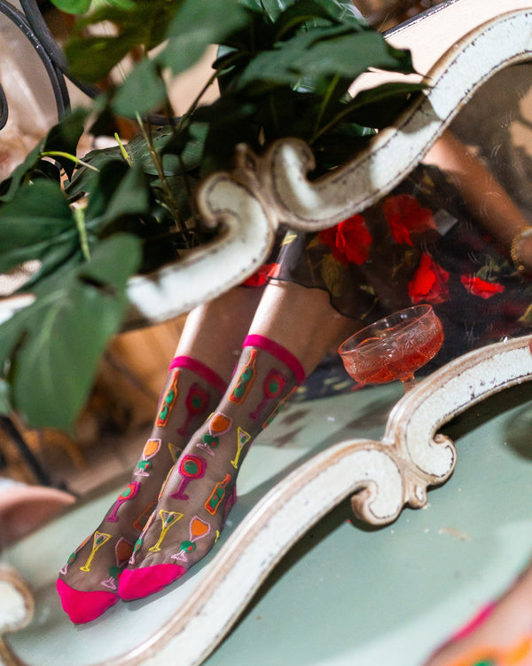 Person wearing colorful cocktail pattern socks with a decorative mirror and plant in the background