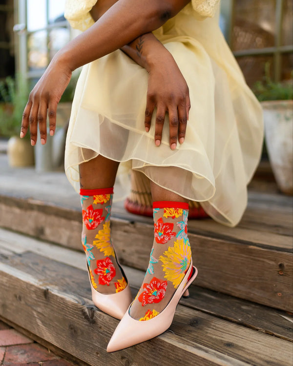 Person wearing colorful floral socks with sheer design, sitting on wooden steps.