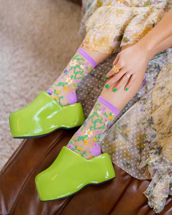 Person wearing green platform shoes with floral-patterned socks on a textured surface.