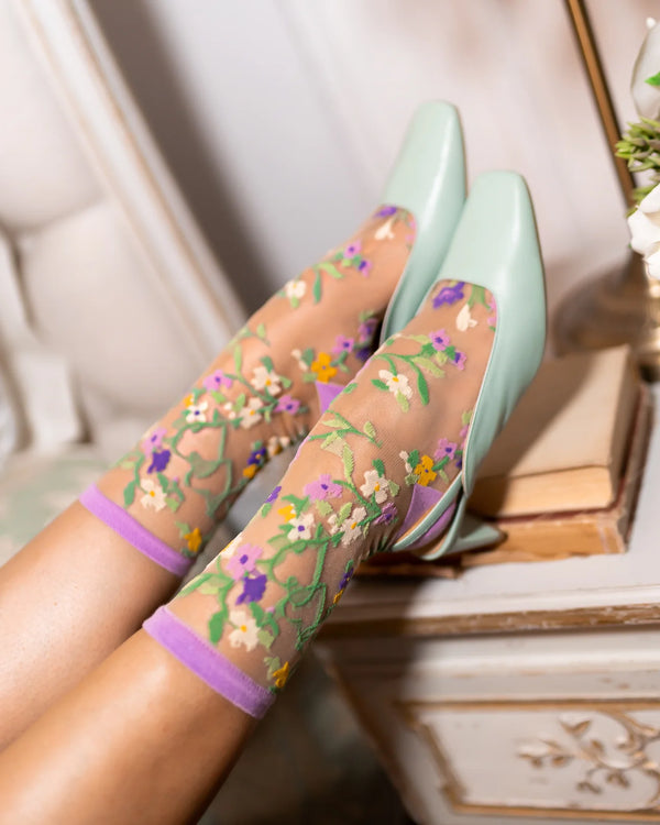 Transparent floral-patterned socks with green and purple accents worn by a person.