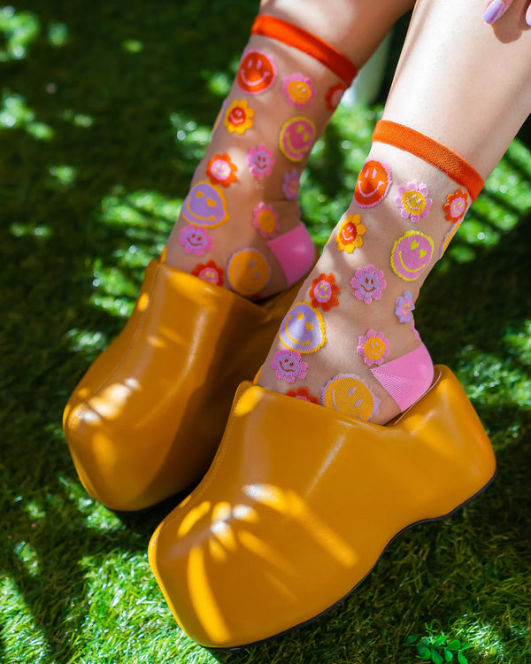 Colorful socks with smiley face patterns worn with yellow clogs on grass.