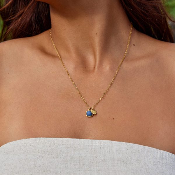 Gold necklace with a blue pendant on a person wearing a light gray top.
