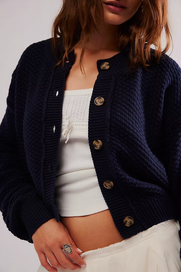 Person wearing a navy blue cardigan over a white top and skirt on a plain background