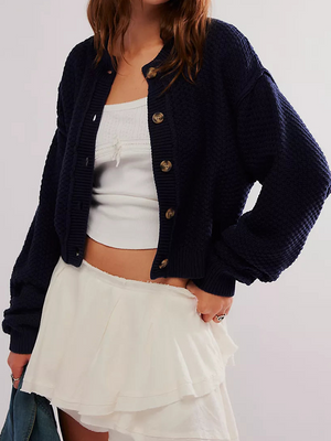 Woman wearing a navy cardigan over a white top and skirt on a plain background