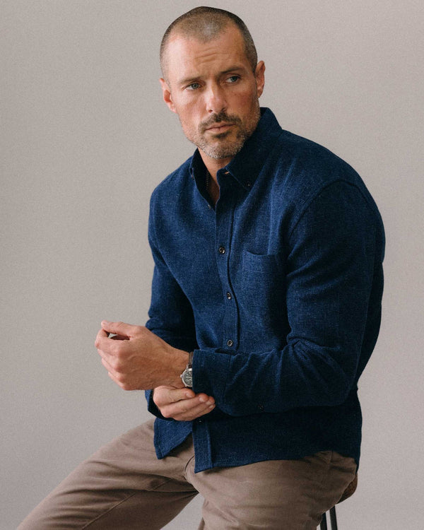 Man wearing a blue shirt and brown pants against a plain background