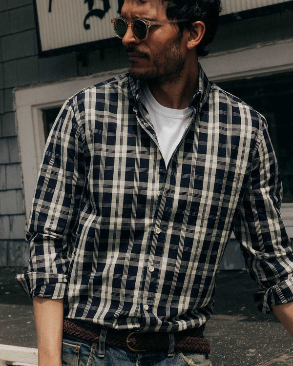 Man wearing a navy and white plaid shirt with rolled-up sleeves, standing outdoors.