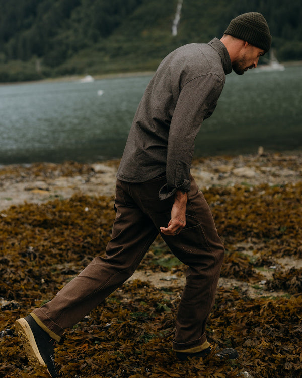 Man walking on a rocky shoreline with a lake and mountains in the background
