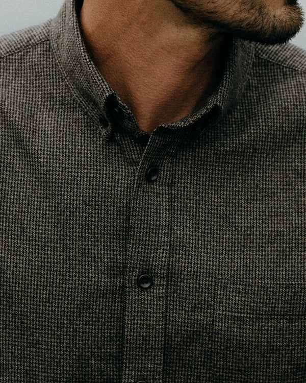 Close-up of a person wearing a dark green and gray checkered shirt with a blurred background